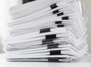 Piles of white papers work large piles of papers stacked together. On the desk in the office with black clip. Documents that are not finished. Business concept.